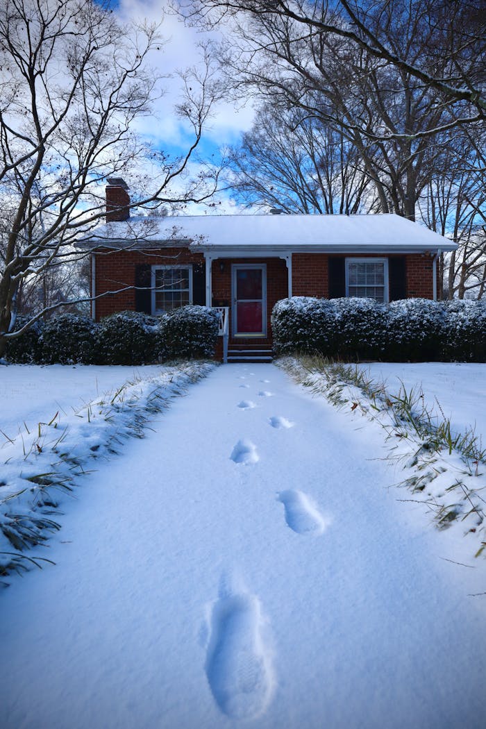 Cozy brick house with snow-covered path and footprints in a serene winter setting.